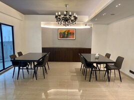 Un salón de conferencias con una larga mesa, sillas, una araña y un cuadro de colores en la pared.