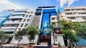 A modern hotel with a prominent glass facade, multiple balconies, and a well-maintained entrance area with palm trees. - Hotel omni residency Baridhara (Dhaka)