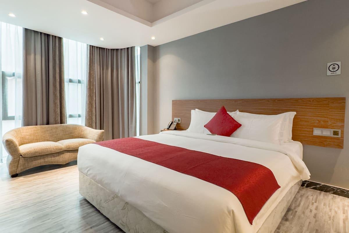 Una habitación de hotel moderna con una cama grande, cabecera de madera, manta roja y suelo de madera.