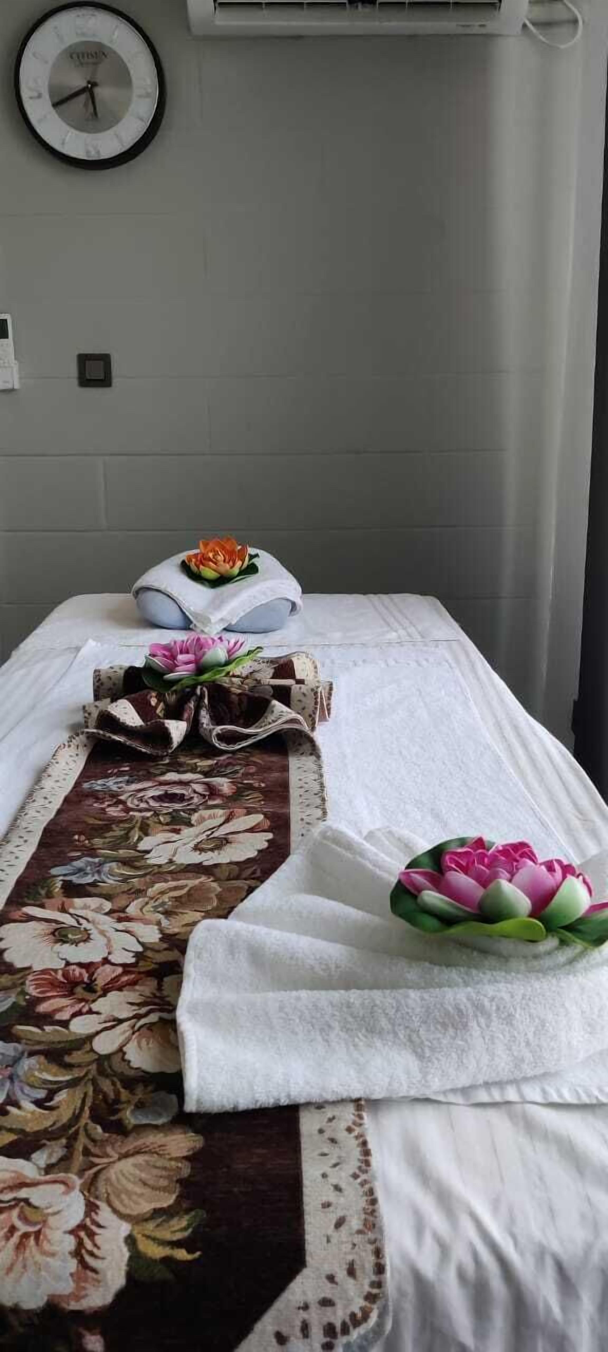 Una cama bien hecha con una colcha estampada con motivos florales, una toalla blanca y una almohada decorativa con una flor.
