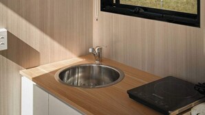 A modern kitchen with a wooden countertop, stainless steel sink, and a window overlooking a forested area. - Tiny Ironbark by Tiny Away (Glenreagh)