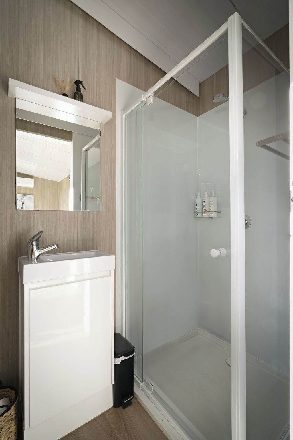 A modern bathroom with a white vanity, a glass shower enclosure, and a mirror above the sink.