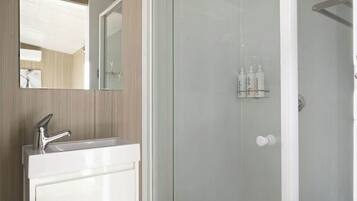 A modern bathroom with a white vanity, a glass shower enclosure, and a mirror above the sink.