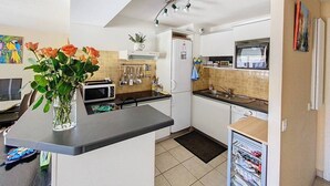 A compact kitchen with a microwave, toaster, sink, and refrigerator. There is a vase with flowers on the counter, and a window above the sink.