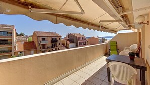 A balcony with a table and chairs, a view of buildings, and a covered area with a chair and a plant.