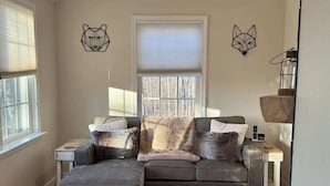 Una sala de estar con un sofá seccional gris, un tapete estampado y dos cuadros con retratos de animales.