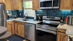 Una cocina con alacenas de madera, refrigerador de acero inoxidable, microondas, horno y barra para café.
