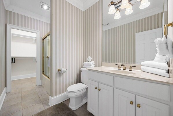 A bathroom with a toilet, sink, and mirror, featuring striped wallpaper and a chandelier. - Lux 5BR Mediterranean-Style Home w/ Private Pool (North Myrtle Beach)