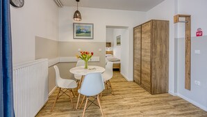 Une pièce moderne avec un plancher en bois, des murs blancs, une table ronde entourée de chaises, une horloge et un tableau encadré.