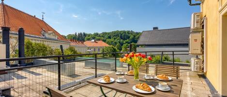 A balcony with a table set for breakfast, a bench, and a view of buildings and trees.