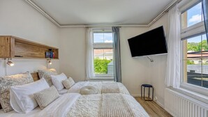 Een slaapkamer met een bed, een televisie, een raam en een plank.