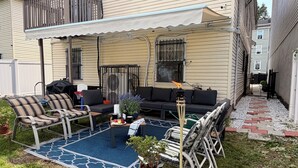 A covered patio with outdoor furniture, a grill, and a small garden area. - Exquisite 3 Bedrooms (Newark)