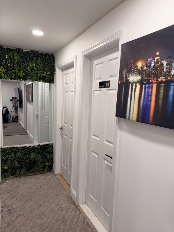 A hallway with white doors, a cityscape mural, and a green plant wall.