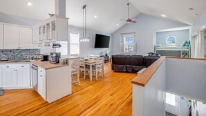 A spacious living area with a dining table, a sofa, and a TV mounted on the wall. - Steps 2Beach~Heated Pool~Hot Tub~MiniGolf~Gameroom! (Panama City Beach)