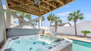 A hot tub with a wooden roof structure, a swimming pool, and palm trees in the background. - Steps 2Beach~Heated Pool~Hot Tub~MiniGolf~Gameroom! (Panama City Beach)