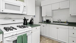 A kitchen with white cabinets, a gas stove, a microwave, and a sink.