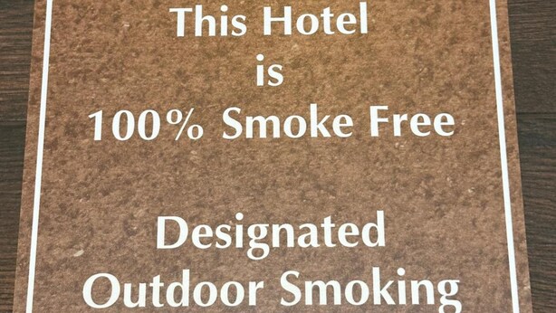 A cork sign stating the hotel is 100% smoke-free with designated outdoor smoking areas. - Stay Inn by OYO Near I 80 Lincoln West (Lincoln)