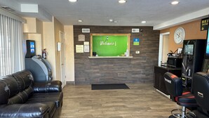 A reception area with a green welcome wall, an ATM, a pet policy notice, a clock, and a cash center. - Stay Inn by OYO Near I 80 Lincoln West (Lincoln)