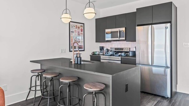 A modern kitchen with a central island, bar stools, stainless steel appliances, and pendant lighting. - FIFA 10 Mins Away | Rooftop | Gym | King bed (Philadelphia)