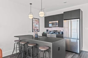 A modern kitchen with a central island, bar stools, stainless steel appliances, and pendant lighting. - FIFA 10 Mins Away | Rooftop | Gym | King bed (Philadelphia)