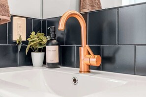 A bathroom sink with a copper faucet, a potted plant, and a bottle of hand soap.