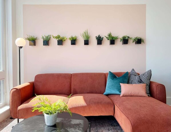 A living room with a red sofa, a coffee table, and a wall-mounted plant shelf.