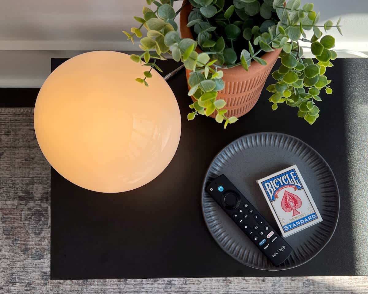 A table with a remote control, a deck of Bicycle playing cards, and a potted plant.