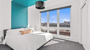 A modern bedroom with a large window, a bed, and a teal accent wall. - FIFA 10 Mins Away | Rooftop | Gym | King bed (Philadelphia)