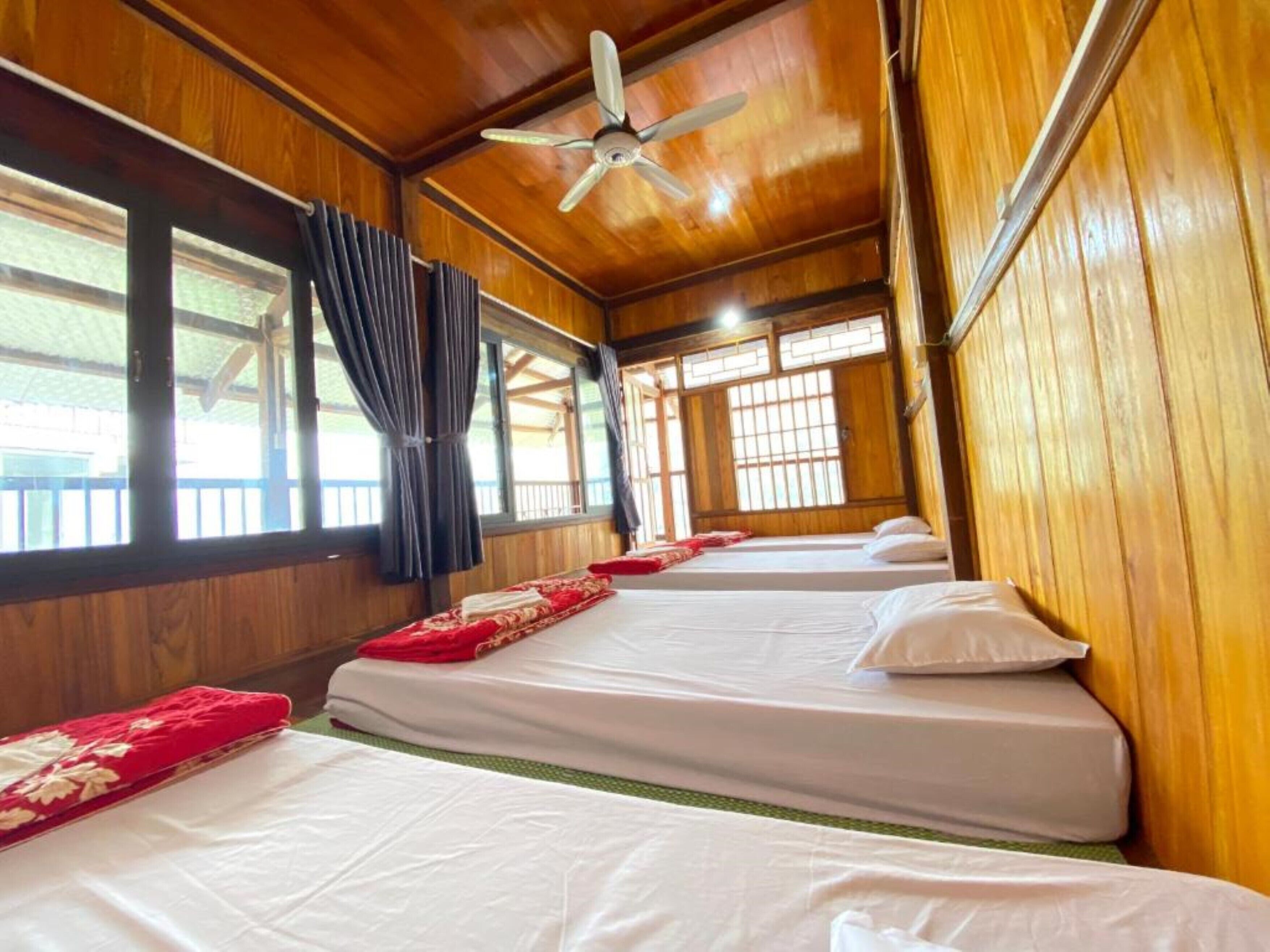 A room with wooden walls and ceiling, multiple beds with white linens, red and white bedding, and a ceiling fan.