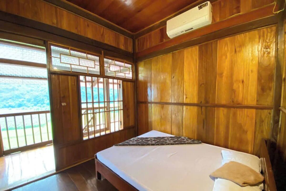 A wooden room with a bed, a window with a view, and an air conditioning unit.