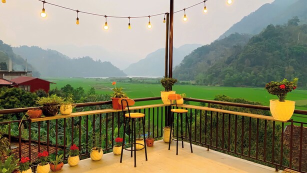 A balcony with potted plants, a chair, and a view of green fields and mountains. - Duy Tuyen Ba Be Homestay Free BBQ (Ba Be)