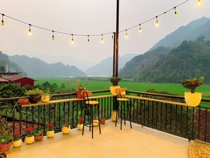 A balcony with potted plants, a chair, and a view of green fields and mountains. - Duy Tuyen Ba Be Homestay Free BBQ (Ba Be)