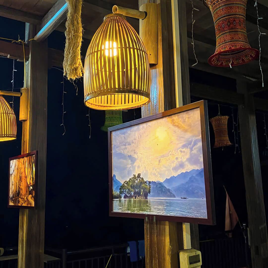 A room with a large framed painting of a sunset over water, hanging on a wooden wall.