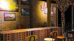 A bar area with a patterned tablecloth, wooden chairs, and framed pictures on the brick walls. - Duy Tuyen Ba Be Homestay Free BBQ (Ba Be)