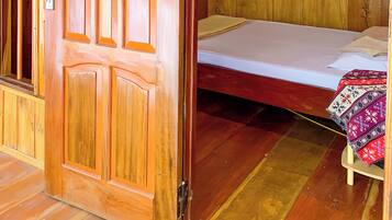 A wooden room with a bed, a small table with a cloth, and a picture on the wall.