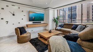 Ein modernes Wohnzimmer mit einem großen Flachbildfernseher, einer Couch, einem Couchtisch und einem großen Fenster mit Blick auf die Stadt.