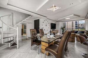 Relax in this open-plan living space with a central dining table and comfortable seating, featuring a contemporary staircase and a large window with city views.