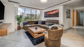Ein modernes Wohnzimmer mit einem Ecksofa, einem Couchtisch und einem großen Fenster mit Blick auf die Stadt.