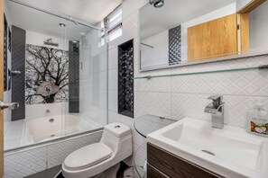 Bathroom features a glass-enclosed shower, white toilet, and sink with a wooden cabinet above.
