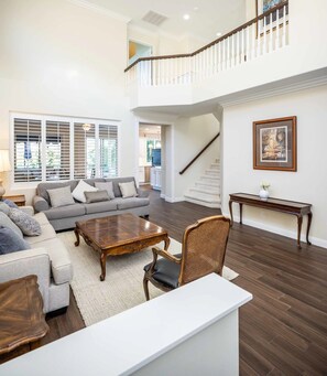 A spacious living room with a grey sofa, wooden coffee table, and a white console table. A staircase leads to an upper level. - Coto De Caza Modern Home, Golf Course View (Coto de Caza)