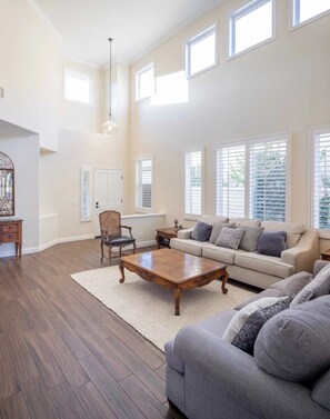 A spacious living room with a high ceiling, large windows, a wooden coffee table, a sofa, and a chair. - Coto De Caza Modern Home, Golf Course View (Coto de Caza)