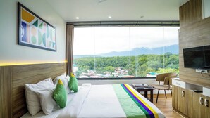 A hotel room with a bed, a television, a desk, and a view of a mountainous landscape. - Treebo White Sand (Dehradun)