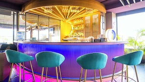 A bar area with a curved counter, teal bar stools, and a variety of bottles. - Treebo White Sand (Dehradun)
