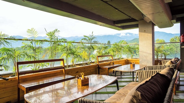 An outdoor seating area with wooden furniture and a view of mountains. - Treebo White Sand (Dehradun)