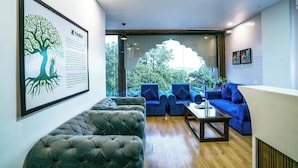 A modern living room with a large window, a framed tree illustration, and blue sofas. - Treebo White Sand (Dehradun)