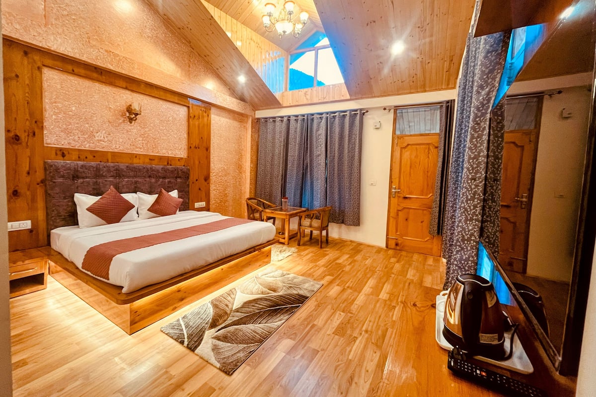 A wooden-floored bedroom with a large bed, a desk, and a coffee maker.