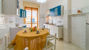 A compact kitchen with white and blue cabinets, a dining table with a yellow tablecloth, and a view of the outside through a glass door. - Casa Gallipolina Sea-View Apt in Gallipoli, Gallipoli, Italy (Gallipoli)
