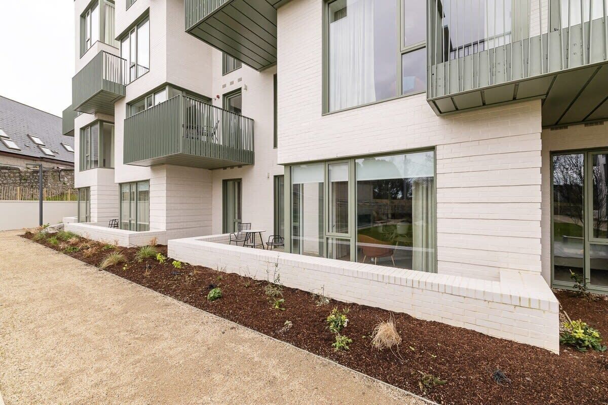 A modern multi-story residential building with balconies, large windows, and a landscaped garden area.