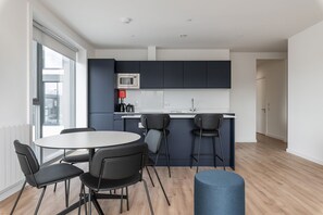 Una cocina moderna con microondas, un fregadero y taburetes de bar. Hay una mesa redonda con sillas y un otoman azul.