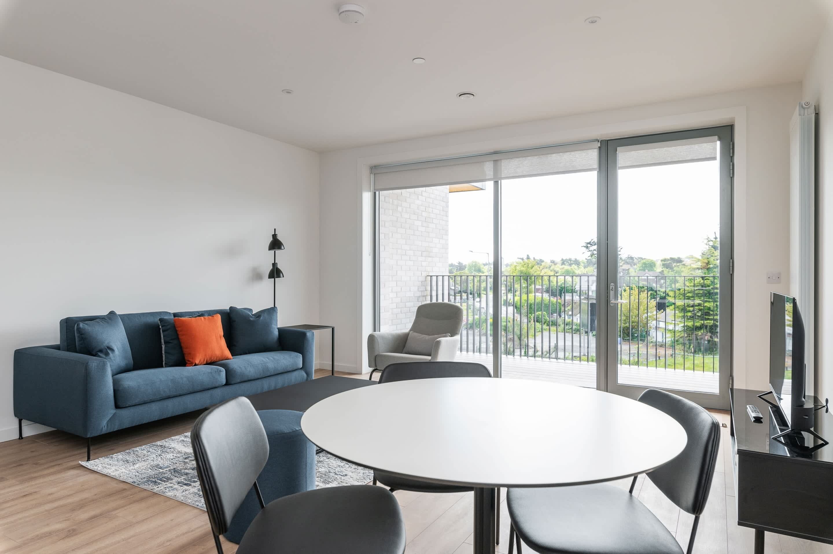 A modern living room with a sofa, chairs, a round table, and a TV.